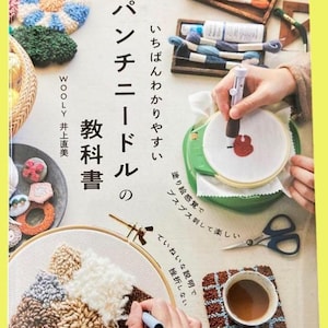 May include: A Japanese language book titled "Punch Needle Textbook" with colorful examples of punch needle art. The image shows a person using a punch needle tool on a fabric stretched in a hoop, along with scissors and a cup of coffee.