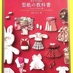 Könnte beinhalten: Ein roter Buchumschlag mit japanischem Text und Miniatur-Puppenkleidung. Der Buchtitel lautet "Obitsu 11 no Katagami no Kyokasho". Das Bild zeigt verschiedene Puppenoutfits, darunter Kleider, Röcke und Jacken, in einer Vielzahl von Farben und Mustern.