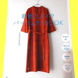 Op de afbeelding: Een boekomslag met een roestkleurige jurk die aan een hanger hangt. De titel van het boek is in het Japans, met de woorden "Perfect Book" in het Engels. Extra Japanse tekst en pictogrammen zijn ook zichtbaar. Het boek staat op een witte achtergrond.