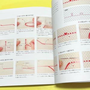 Puede incluir: Libro abierto con ilustraciones detalladas de t&eacute;cnicas de bordado. Las p&aacute;ginas muestran instrucciones paso a paso con hilo rojo sobre tela beige. Diagramas y texto japon&eacute;s acompa&ntilde;an las gu&iacute;as visuales, demostrando varios m&eacute;todos de puntada.