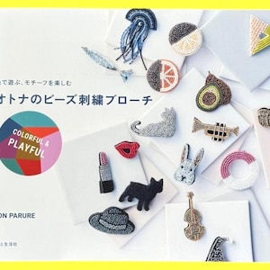 May include: A collection of colorful, beaded brooches in various shapes, including a cat, rabbit, lipstick, and musical instruments. The brooches are displayed on white squares, with text in Japanese and the words "COLORFUL & PLAYFUL".