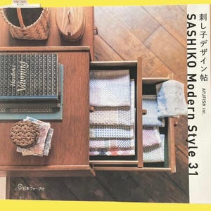 May include: A wooden cabinet with open drawers displaying folded textiles. A stack of books and a woven basket sit on top. The book spines read "Vauning Handbook". The text "SASHIKO Modern Style 31" is visible on the right side.