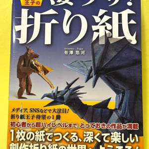 May include: A book cover featuring origami art. The title is in Japanese characters, with the words "Origami" and "Prince" in English. The cover showcases origami figures, including a dragon and a person holding a bird. Text in Japanese is also present.
