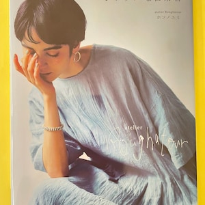 以下が含まれることがあります： atelier Roughatourの細野由美による書籍「シンプルな日常着」。表紙には、丸首で半袖のライトブルーの質感のあるゆったりとしたドレスを着用した人物が、無地の背景の前に写っています。