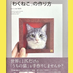 May include: A book cover featuring a framed wool felt cat portrait. The book title is in Japanese, with English translations below. The cover also includes text about making a cat from wool felt, with a smaller image of a cat and a list of cat breeds.