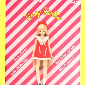 May include: A magazine cover with a red and white striped background features a doll in a red dress with a bow. The magazine title reads "Dollybird" and "Tiny Dolls". Additional text includes "vol.22", and names like "Doran Doran".