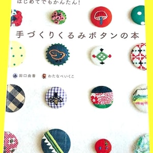 Può includere: Copertina di un libro con una collezione di bottoni fatti a mano, rotondi e colorati, decorati con vari motivi e disegni. È presente del testo giapponese, insieme al titolo "Libro di bottoni fatti a mano".
