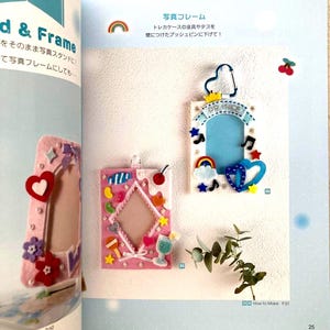 May include: Three decorative photo frames in a craft book. The frames are pink and decorated with felt shapes like hearts, stars, and rainbows. One frame has the text "BIG PEACE". The frames are displayed on a light blue background.