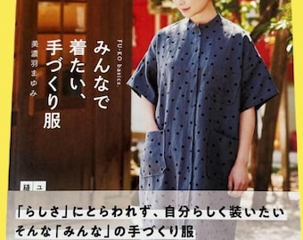Può includere: Una donna indossa una camicia blu navy a pois neri, in posa davanti a una copertina di un libro con testo giapponese. La copertina del libro mostra il titolo "Abiti fatti a mano per tutti".