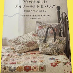 Op de afbeelding: Boekomslag met de titel "Wonderful quilt life in my 70s" door Sanae Kono. De afbeelding toont een quilt, kussens en een tote bag met bloemmotieven. De quilt heeft een bloemenontwerp met rode, roze en blauwe bloemen.