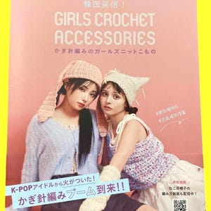 May include: A magazine cover featuring two women modeling crochet accessories. The title reads "GIRLS CROCHET ACCESSORIES" in large letters. The cover also includes Japanese text and images of crochet hats, sweaters, and arm warmers. The background is a soft pink.