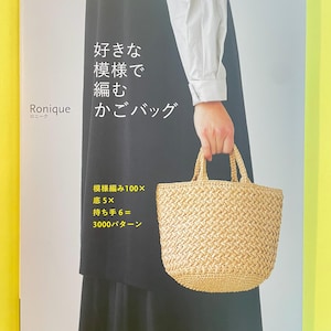 Può includere: Un libro di istruzioni con copertina flessibile intitolato Ronique con testo giapponese sulla copertina. La copertina presenta una fotografia di una borsa a cestino intrecciata color beige chiaro con due manici, tenuta contro un indumento scuro e una camicia a maniche lunghe.