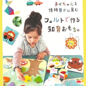May include: A craft book cover titled applemints featuring various felt toys including a train, a geometric cat, a cube, and a lion. The cover displays Japanese text and shows a person interacting with a felt play mat featuring a tree and shapes.