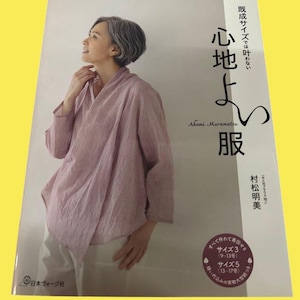 May include: A book cover featuring a woman in a pink top and white pants. The title is in Japanese characters, with the author's name, Akemi Muramatsu, below. The book is from the Heart Warming Life Series.