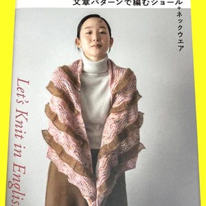 May include: A woman wearing a pink and brown shawl over a white turtleneck sweater. The book cover in the image reads "Let's Knit in English!" and features Japanese text. The shawl has a ruffled design.