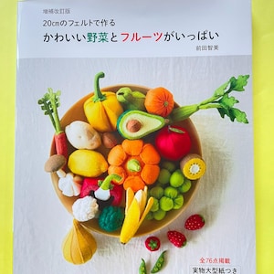 May include: A craft book titled 20cmのフェルトで作る かわいい野菜とフルーツがいっぱい featuring a bowl filled with various colorful felt vegetables and fruits, including a yellow pepper, orange pumpkin, avocado, red apple, and green grapes.