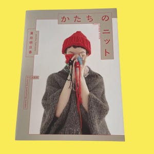 以下が含まれることがあります： 赤いニット帽と灰色のニットショールを着て、カラフルな糸を持っている人の表紙。本のタイトルは日本語で、英語で「funny shape knits」と書かれています。著者の名前も表示されています。