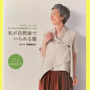 Puede incluir: Portada de libro con una mujer sonriente vestida con un top cruzado claro y una falda marrón. El título japonés se traduce como "Ropa con la que puedo ser yo misma". La portada también incluye texto en japonés y tallas S, M, L, 2L y 3L.
