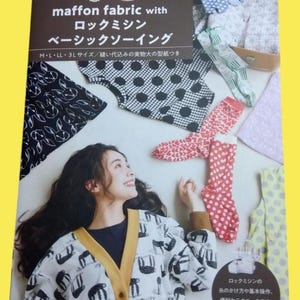 以下が含まれることがあります： 生地サンプルとソーイングブックを持つ女性。本には「maffon fabric」とソーイング技術の広告が日本語と英語で書かれています。女性は白いカーディガンを着ており、黒いナマケモノの模様があります。