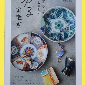 May include: A book cover featuring Japanese text and images of repaired ceramic plates. The plates are decorated with intricate patterns and gold accents. The book's title is in Japanese, with additional text promoting the art of kintsugi.