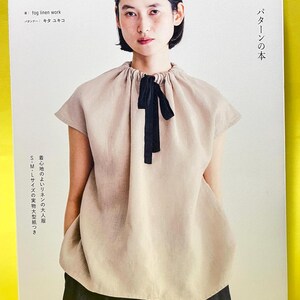 以下が含まれることがあります： FOG LINEN WORKと日本語のタイトルが記された書籍の表紙。ギャザーネックと黒いリボンタイが付いたベージュのノースリーブトップスを着用した人物と、ダークカラーのスカートが写っている。表紙には出版社名KADOKAWAが記載されている。