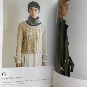May include: A page from a craft book featuring a black and white houndstooth neck warmer worn over a cream-coloured textured jumper. The text includes the letter G, the Japanese title 千鳥格子のネックウォーマー, and instructions referencing page 33.