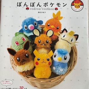 Op de afbeelding: Een boek getiteld "POMPOM POKÉMON" met verschillende kleurrijke Pokémon-personages van pompons. De personages zijn gerangschikt in een geweven mand. De boekcover heeft Japanse tekst en illustraties van de personages.