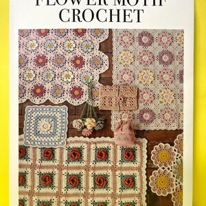 以下が含まれることがあります： MARUN CROCHET FLOWER MOTIF CROCHETというタイトルの手芸本。ピンク、黄色、青、緑の色合いで編まれたブランケット、小さなポーチ、花柄のモチーフなどが木製の表面に配置されている様子が写っている。