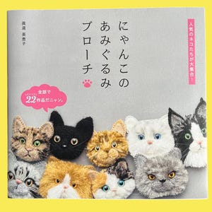 May include: A book cover featuring a collection of crocheted cat brooches in various colors and patterns. The title is in Japanese, with additional text indicating 22 projects. The background is a light gray.