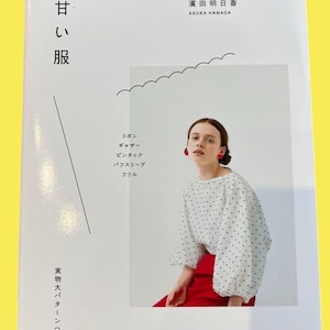 以下が含まれることがあります： 白い水玉模様のブラウスと赤いスカートを着た女性の写真が掲載された、日本語のテキストが入った本の表紙。 本のタイトルは「甘い服」で、リボン、ギャザー、パフスリーブなどのデザイン要素が特徴です。