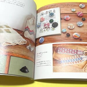 Puede incluir: Un libro abierto muestra botones hechos a mano y accesorios bordados. Una bolsa blanca y una bolsa peque&ntilde;a con patrones geom&eacute;tricos est&aacute;n sobre una superficie de madera. La p&aacute;gina tambi&eacute;n muestra diademas.
