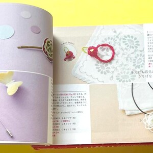 Puede incluir: P&aacute;gina de un libro de manualidades que muestra accesorios hechos a mano. Se incluyen una horquilla, un broche de mariposa, un anillo rojo y un collar con un colgante de flor. La p&aacute;gina tiene texto en japon&eacute;s y est&aacute; sobre un fondo lila claro.