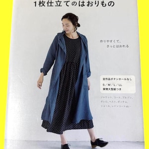 以下が含まれることがあります： 青いダスターコートと黒い水玉模様のドレスを着た女性が写っている本の表紙。日本語のテキストは「1枚仕立てのはおりもの」と書かれており、パターンとサイズに関する詳細が含まれています。