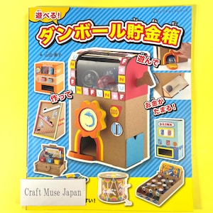 以下が含まれることがあります： 「ダンボール貯金箱」というタイトルの書籍の表紙。日本語で「ダンボール貯金箱」は「Cardboard Piggy Bank」を意味します。表紙には、ガムボールマシン、シューティングゲーム、スロットマシンなど、さまざまな段ボール製の貯金箱のカラフルなイラストが描かれています。この本は日本語で書かれており、Craft Muse Japanシリーズの一部です。