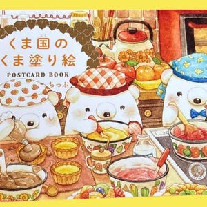 以下が含まれることがあります： 「くま国のくま塗り絵」というタイトルのポストカードブック。キッチンで料理をする3頭の白いクマのカラフルなイラストが描かれています。クマたちは柄入りのバンダナを頭に巻き、生地の入ったボウルや果物、調理器具に囲まれています。