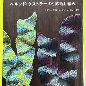 Può includere: Copertina di un libro con esempi di progetti a maglia nei toni del verde, blu e viola. Il titolo è in giapponese, con le parole "Bernd Kestler's Turn Back Knitting" in bianco. La copertina include anche testo su sciarpe, scialli e gonne.