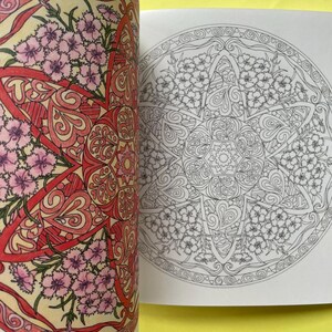 May include: A coloring book featuring a circular mandala design with floral and heart patterns. The left page is colored in shades of pink, red, and yellow, while the right page displays the same intricate line art in black and white on paper.
