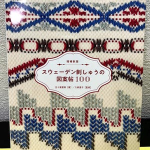 Può includere: Copertina di un libro con un motivo ricamato dettagliato in blu, rosso e grigio su sfondo crema. Il titolo in giapponese è "Swedish Embroidery Pattern Book 100". Il testo giapponese indica un'edizione aggiornata.