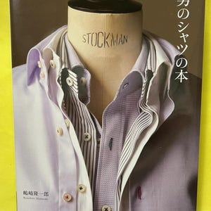 May include: A book cover featuring a mannequin head wearing several button-down shirts. The shirts are various shades of purple and white, with striped and solid patterns. The word "STOCKMAN" is visible on the mannequin. Japanese text is present.