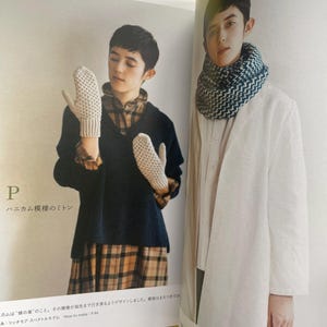 May include: A page from a craft book showing two knitted items. On the left, a pair of off-white honeycomb-patterned mittens. On the right, a thick, textured infinity scarf featuring a blue and white chevron-style knit pattern.