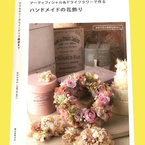 Op de afbeelding: Een boekomslag met handgemaakte bloemstukken, waaronder een krans en kleine boeketten. Een roze doos met "MAGNIFIQUE" is zichtbaar. De tekst op de omslag is in het Japans.