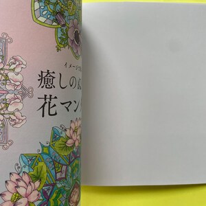 May include: A coloring book page featuring intricate floral mandala designs with pink lotus flowers, purple anemones, and green leaves. The Japanese text "癒しの花マンダラ" is printed in black ink on the left side of the page, which is partially open.