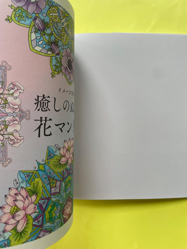 May include: A coloring book page featuring intricate floral mandala designs with pink lotus flowers, purple anemones, and green leaves. The Japanese text "癒しの花マンダラ" is printed in black ink on the left side of the page, which is partially open.