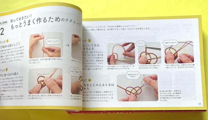 Puede incluir: Libro abierto con texto japon&eacute;s e ilustraciones paso a paso que demuestran t&eacute;cnicas de anudado. Las p&aacute;ginas est&aacute;n amarillentas y las im&aacute;genes muestran manos manipulando cuerdas para crear nudos intrincados. El texto est&aacute; en japon&eacute;s.