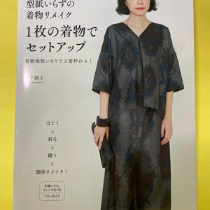 Op de afbeelding: Een instructieboek met zachte kaft en een witte omslag met Japanse tekst en een foto van een persoon in een donkergrijze tweedelige set met een blauw en bruin botanisch patroon. De kaft bevat diagrammen en tekst over naaitechnieken.