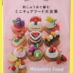 May include: A pink book cover showcasing crocheted miniature food, such as cakes and fruit tarts. The cover includes Japanese text and the English title "Miniature Food". The book is titled "Miniature Food Complete Collection".