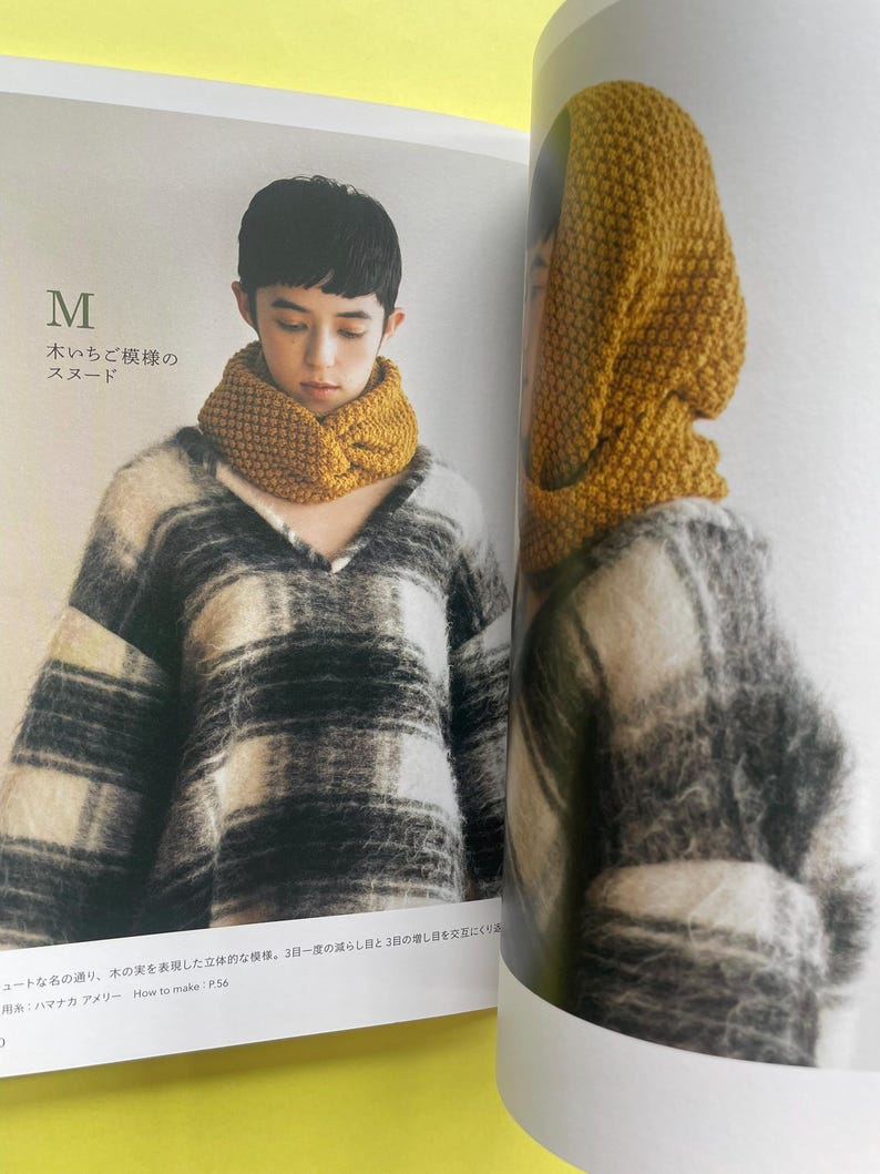 May include: A mustard yellow knitted snood with a textured, bumpy stitch pattern worn around the neck. The snood is featured in a book page alongside a black and white plaid, fuzzy, long-sleeved sweater. The text M and Japanese characters are visible.