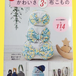 May include: A book cover featuring three fabric bows with yellow and blue floral patterns. The text on the cover is in Japanese, with the words "kawaisa 3 times" and "114 points" visible. Additional images of fabric items are shown.