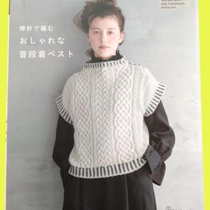 May include: A book cover featuring a woman wearing a white cable-knit vest. The vest has a high neck and striped trim. The book title is in Japanese, with the brand name "applemints" at the top.