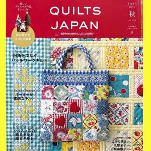 May include: The cover of "QUILTS JAPAN" magazine features a patchwork tote bag with a blue and white handle. The magazine has a red background with white text and Japanese characters. The cover also includes text about Christmas quilts and a special autumn issue.